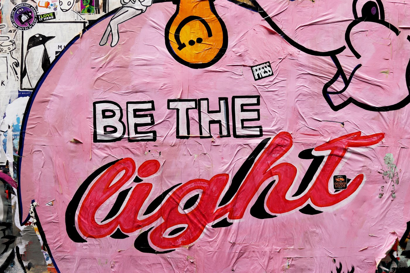 Es ist eine Wand mit Stickern zu sehen, im Mittelpunkt steht dabei ein pinker Elefant, welcher die Aufschrift, 'Be the light' trägt.