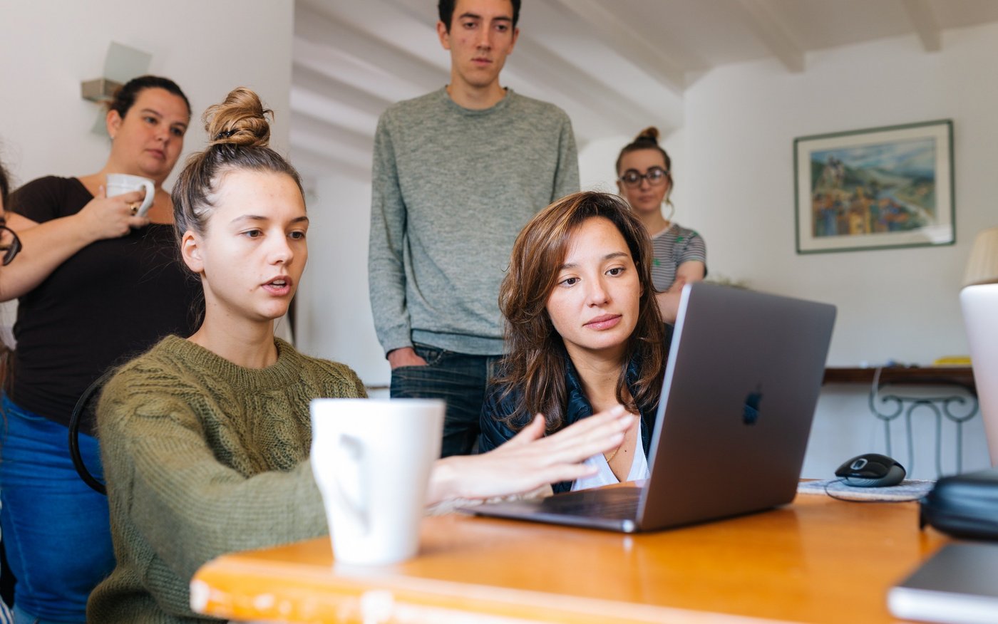 Junge Frau erklärt ihren Teammitgliedern am Notebook einen Sachverhalt.