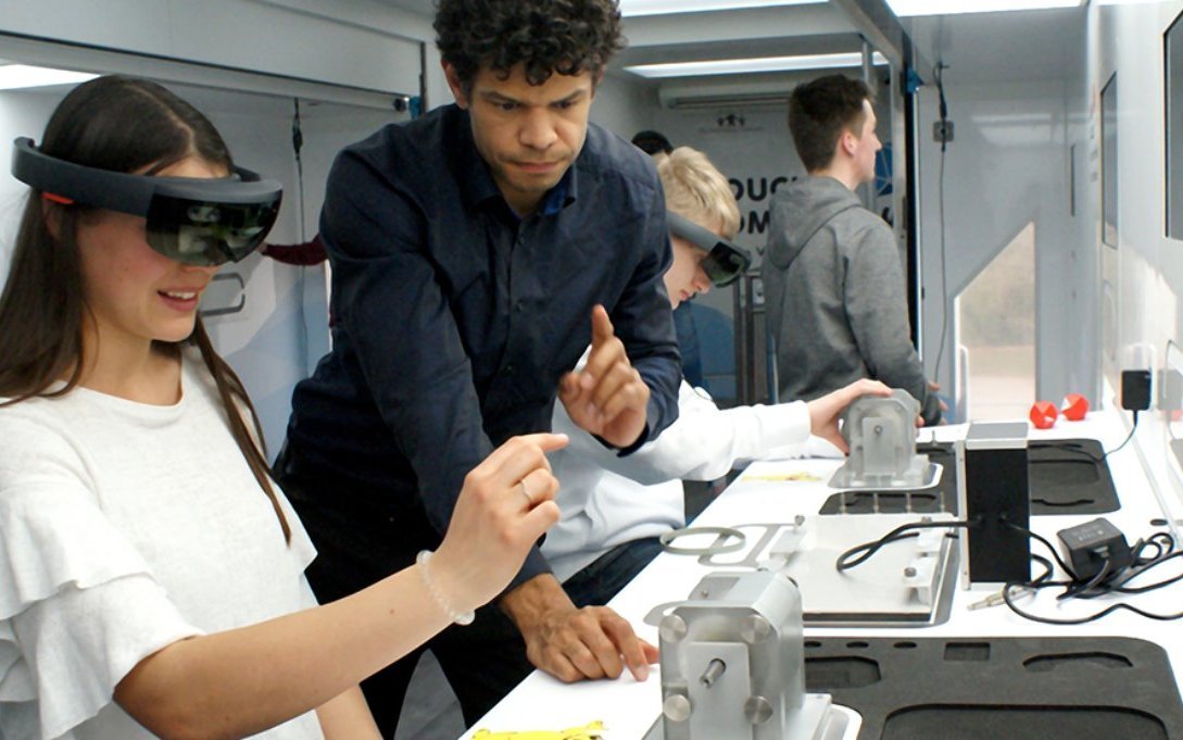Foto: IW Medien Schüler im Inneren des TouchTomorrow-Trucks. Eine Schülerin benutzt eine Augmented Reality Brille zur Erkundung eines Werkstücks.