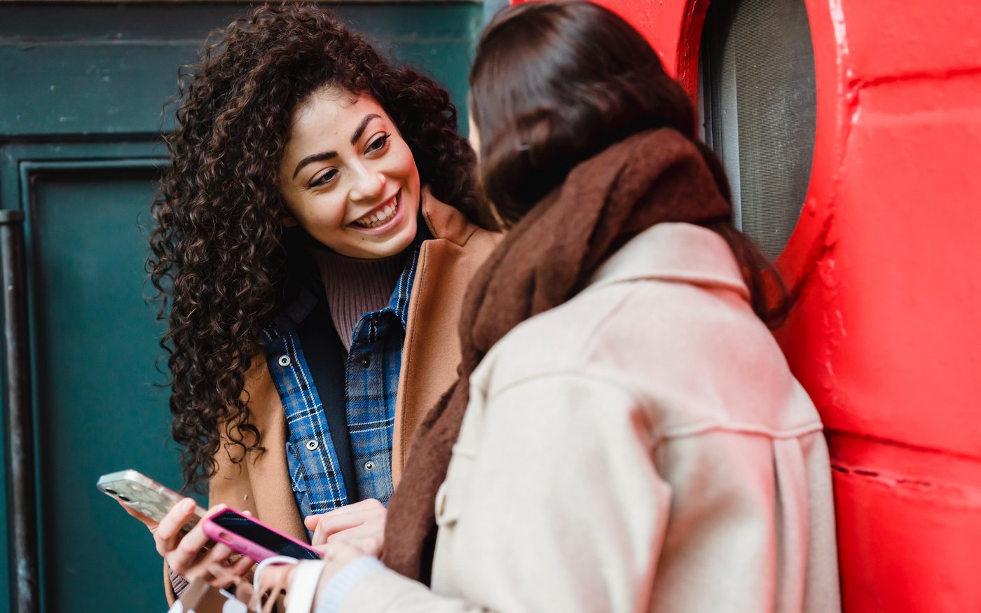 Zwei Frauen stehen vor eine Tür und unterhalten sich angeregt. Dabei halten beide ihr Smartphone in der Hand.