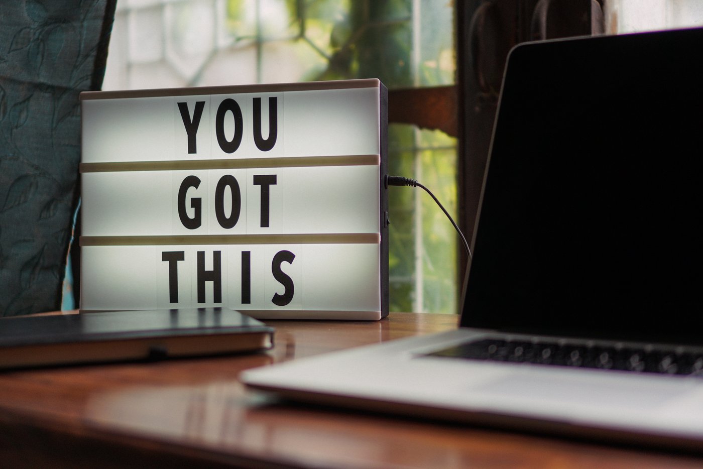 Ein Laptop mit schwarzem Bildschirm auf einem Tisch. Daneben steht ein Leuchtschild mit dem Text - You got this.