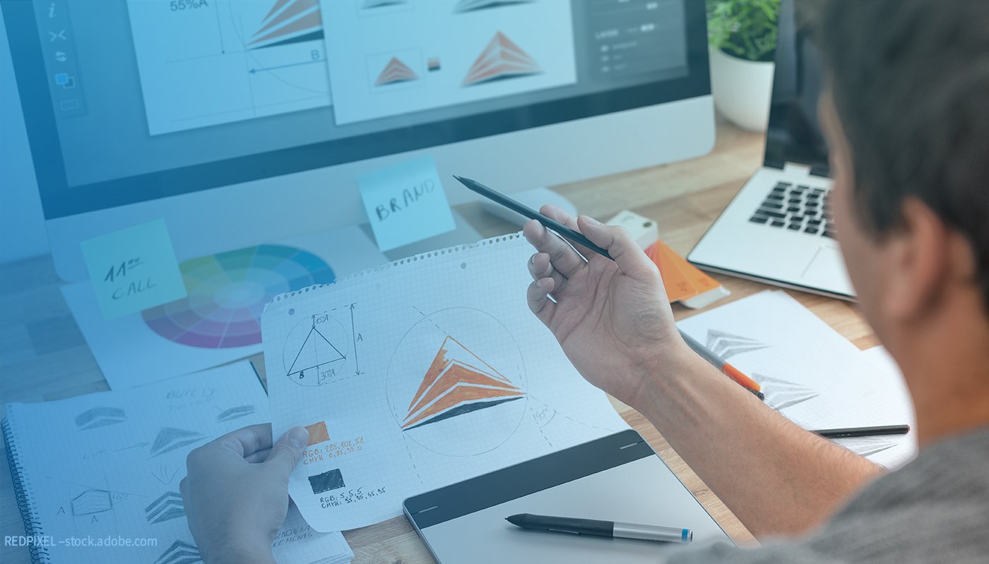 Eine Person hat einen Stift und ein Blatt Papier in der Hand. Auf dem Blatt sind die Dimensionen eines Dreiecks zu erkennen, sowie zwei Farbwerte. Aus diesen Faktoren wurde ein Logo gescribbelt.