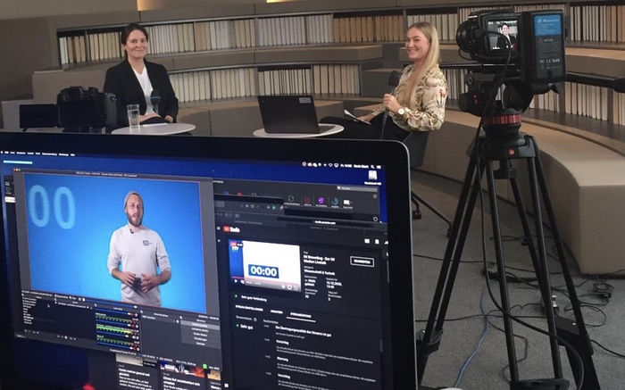 Videodreh im Innenraum mit Blick auf den Videobearbeitungsmonitor, die Kamera sowie auf die Interviewsituation mit zwei Personen.