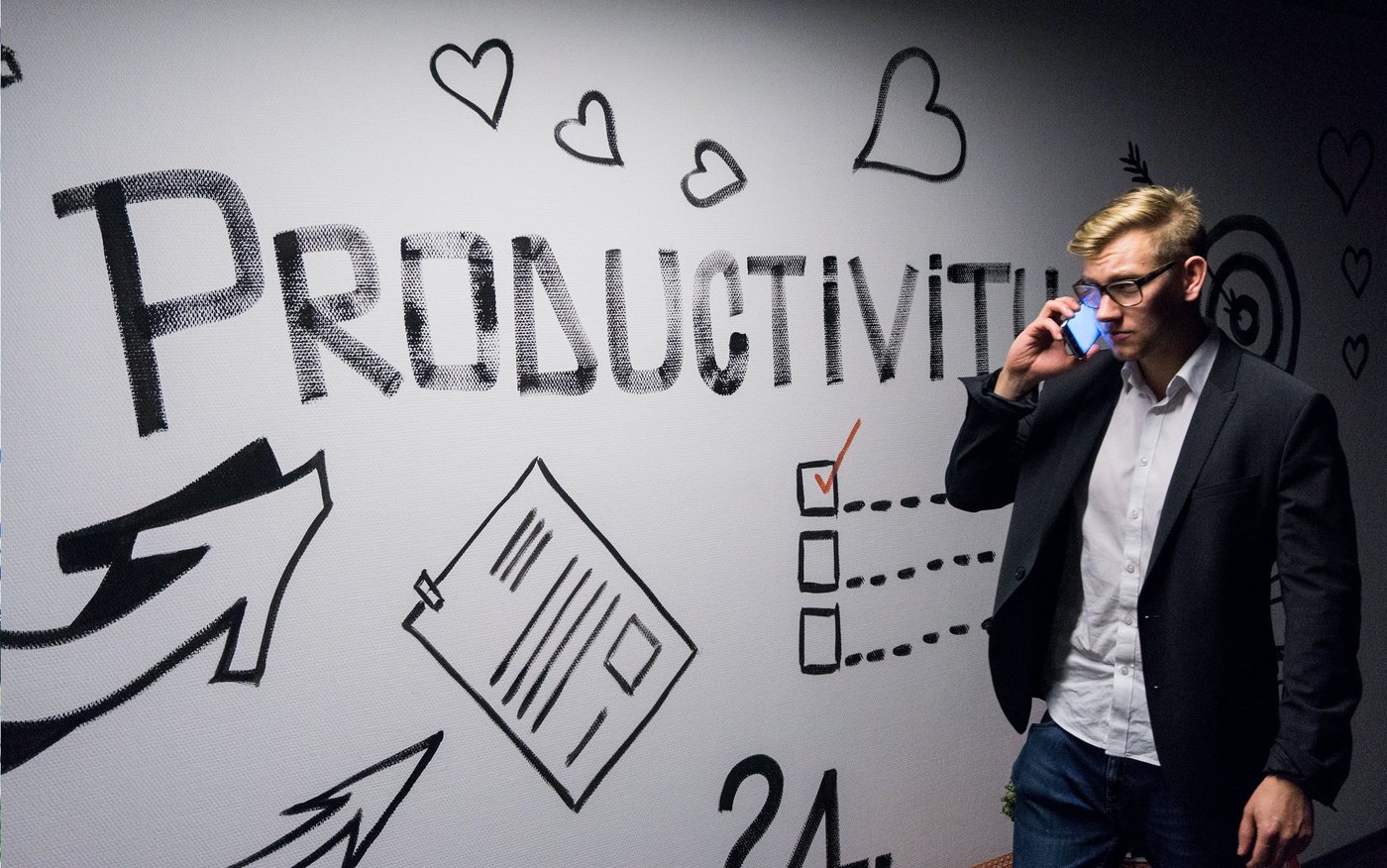 PESO-Modell Ein Mann mit Brille steht telefonierend vor einer Wand, welche mit dem Wort Productivity beschriftet ist.